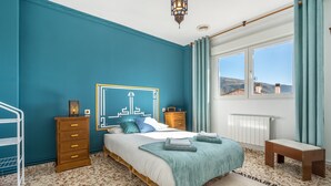 Een slaapkamer met een bed, een houten dressoir, een nachtkastje en uitzicht op het omliggende landschap.