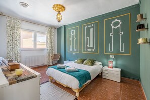 A bedroom with a bed, bedside tables, a chair, a window, and decorative wall art.