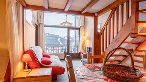 A cozy room with a bed, a table with a basket, and a view of mountains through a large window.