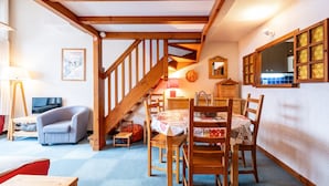 A cozy room with a wooden staircase, a dining table with chairs, a sofa, and a television.