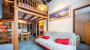 A cozy room with a bunk bed, a sofa with red cushions, a dining area, and a framed picture on the wall.