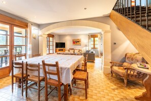 A dining area with a large table and chairs, a sofa, a TV, and a staircase.