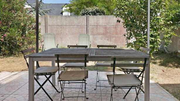 An outdoor patio with a table and chairs, surrounded by a stone-tiled floor and a brick wall.