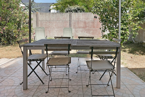 An outdoor patio with a table and chairs, surrounded by a stone-tiled floor and a brick wall.