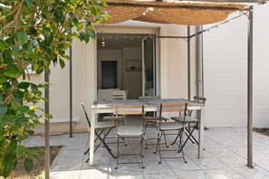 An outdoor patio with a table and chairs, a pergola, and a view into the house.
