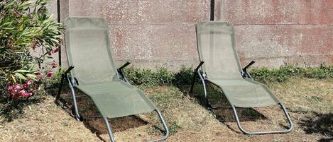 Two green lawn chairs with metal frames, positioned on a grassy area with a concrete wall in the background.