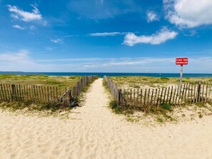 A sandy beach path leading to the sea with a sign indicating the area is not supervised.