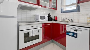A kitchen with white appliances, red cabinets, and a window.