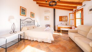 Un dormitorio con cama, mesitas de noche, un banco, sofá, candelabro y cuadros enmarcados en las paredes.