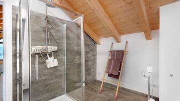 Un baño moderno con cabina de ducha de vidrio, vigas de madera en el techo y una escalera de madera apoyada en la pared.
