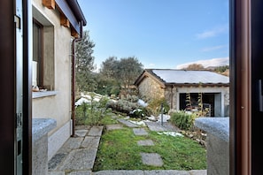 A stone pathway leading to a rustic building with a sloped roof, surrounded by greenery and a clear sky.