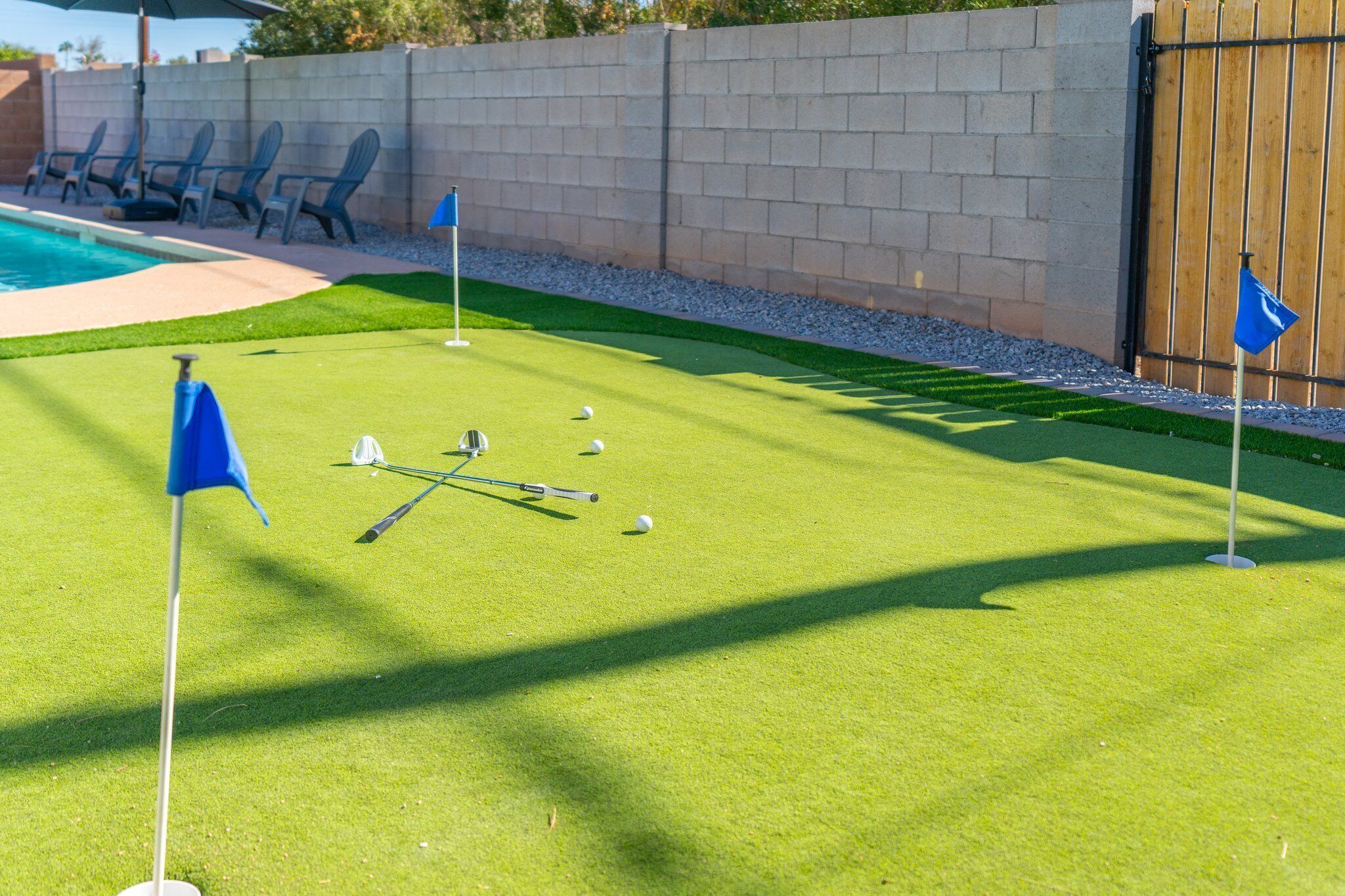 A well-maintained putting green with a flagstick, golf balls, and a wooden fence in the background.