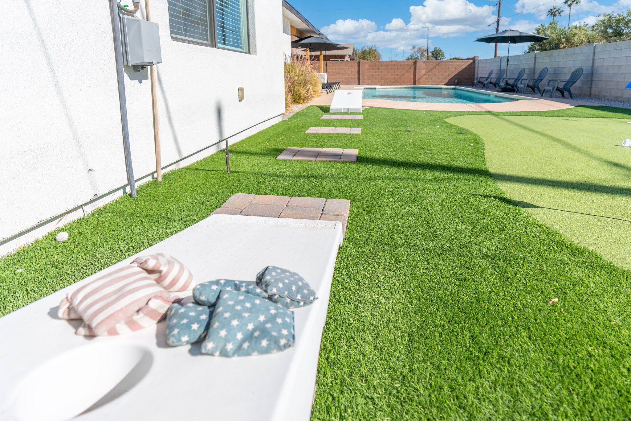A backyard with a swimming pool, a white lounge area with pillows, and a brick pathway.