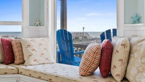 Une vue sur la mer depuis une fenêtre, avec un banc rembourré, des décorations en forme d’étoiles de mer et une chaise bleue.