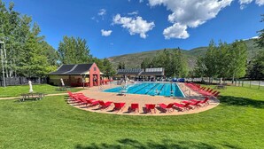 Una piscina con sillas rojas y un pabellón, rodeada de césped y árboles.