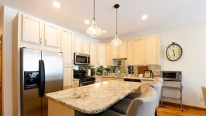 Una cocina moderna con armarios blancos, electrodomésticos de acero inoxidable, encimera de granito e iluminación colgante.