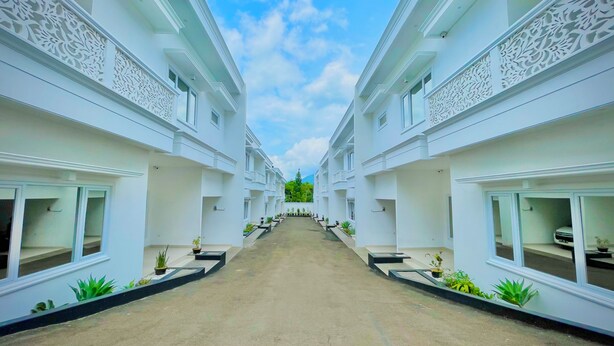 A corridor between two white buildings with balconies, potted plants, and a clear sky. - RRR Luxury Villas (Cisarua)