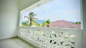 A balcony with a decorative white railing, a clear view of a red-tiled roof, and palm trees in the background. - RRR Luxury Villas (Cisarua)