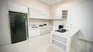 A modern kitchen with white cabinetry, a black refrigerator, a gas stove, and a sink. - RRR Luxury Villas (Cisarua)