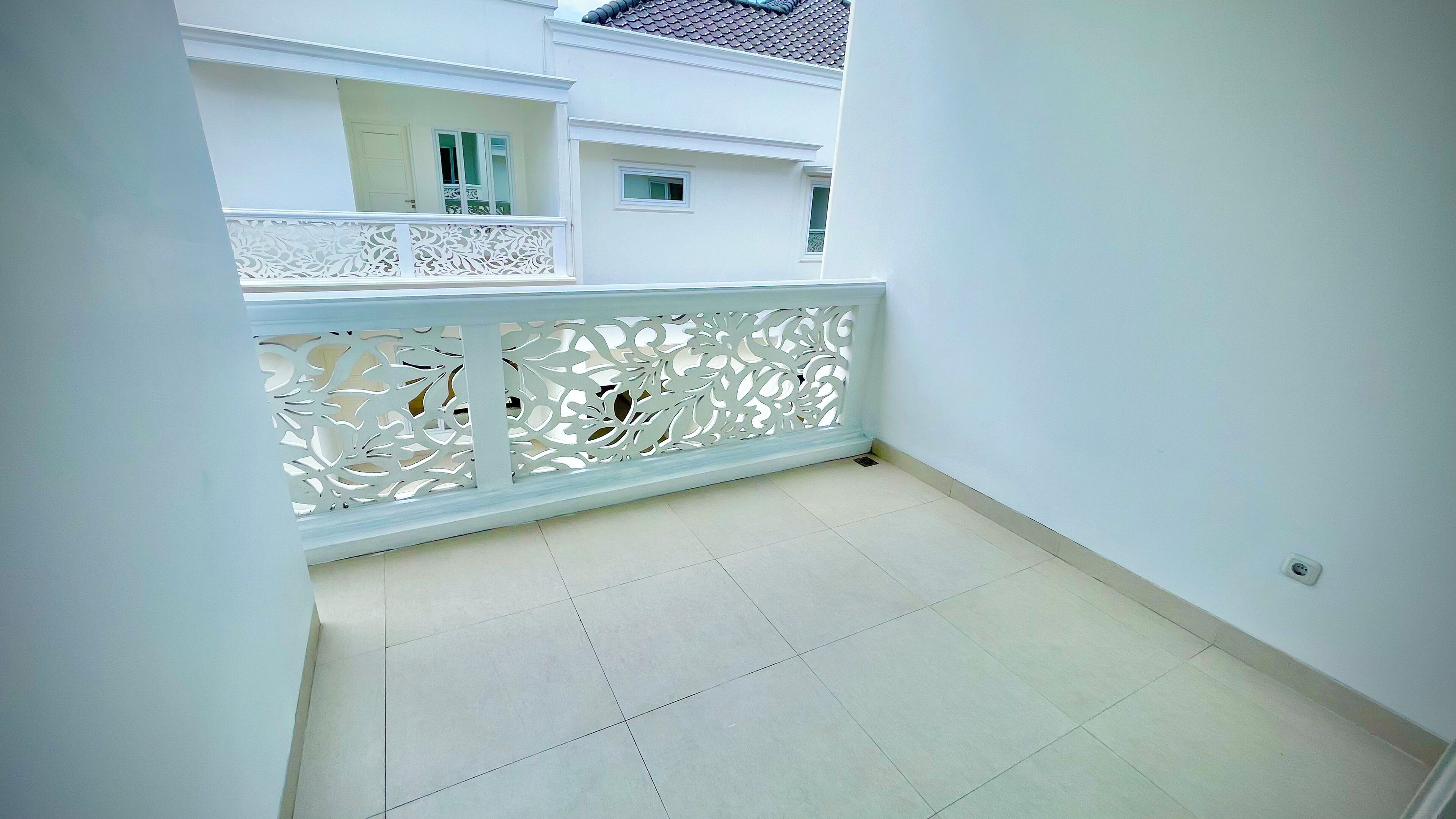 A clean, white balcony with a decorative white railing and a tiled floor.