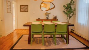 Un comedor con una mesa de madera, sillas verdes, una lámpara de fibra natural, un espejo y una planta en maceta.
