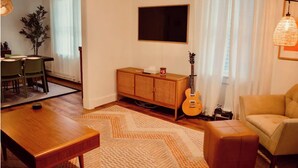 Una sala de estar con una mesa de centro de madera, un sofá, un televisor montado en la pared y una guitarra apoyada contra la pared.
