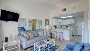 A living room with a sofa, coffee table, and a TV. There is a kitchen area with a microwave, stove, and cabinets. - El Matador 620 -  FREE TICKETS!! Your stay includes free tickets to many area attractions! (Fort Walton Beach)