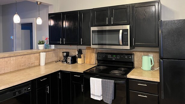 Una cocina moderna con gabinetes negros, electrodomésticos de acero inoxidable y encimera color beige.