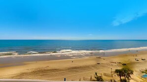Une vue sur la plage, avec un ciel dégagé, du sable et l’océan.