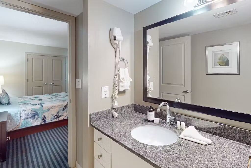 A hotel bathroom with a sink, mirror, hairdryer, and towel rack.