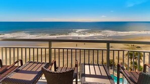 Un balcon avec des fauteuils en osier et une vue sur la plage et l’océan.
