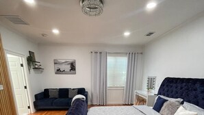 A modern bedroom with a large bed, a dark blue upholstered bench, a white sofa, and a small table with a mirror. -  4-bedroom house / 2 suite. Total 3 amazing  bathrooms Marietta with AC, WiFi (Marietta)