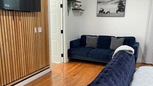 A modern living room with a dark blue sofa, a wooden panel wall, a mounted TV, and a framed landscape painting. -  4-bedroom house / 2 suite. Total 3 amazing  bathrooms Marietta with AC, WiFi (Marietta)