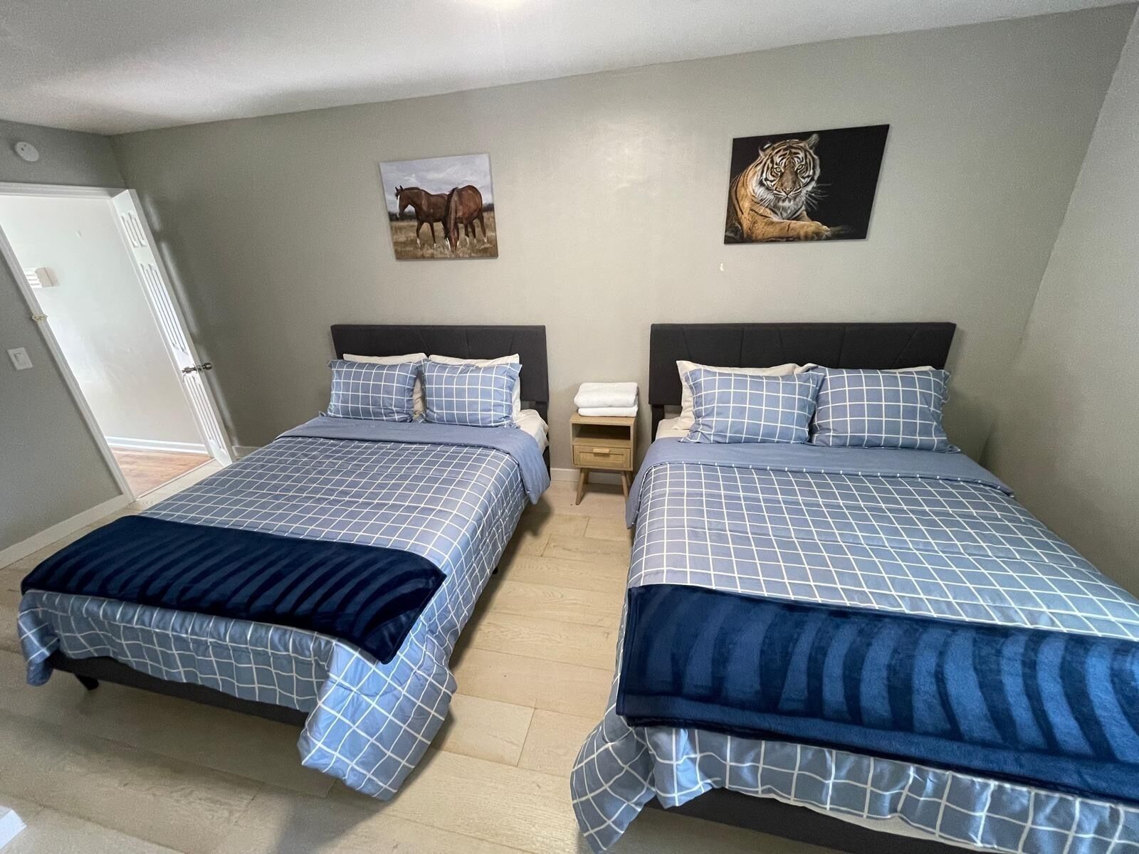 A bedroom with two beds, each with a blue and white checkered bedspread and matching pillows. There are two paintings on the wall, one of a horse and one of a tiger.