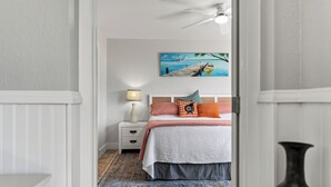 Un dormitorio con una cama, mesita de noche, lámpara y un cuadro de un barco en el agua.