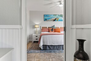 A bedroom with a bed, nightstand, lamp, and a painting of a boat on water.