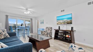 A modern living room with a sofa, a coffee table, a TV mounted on the wall, and a view of the city through large windows.