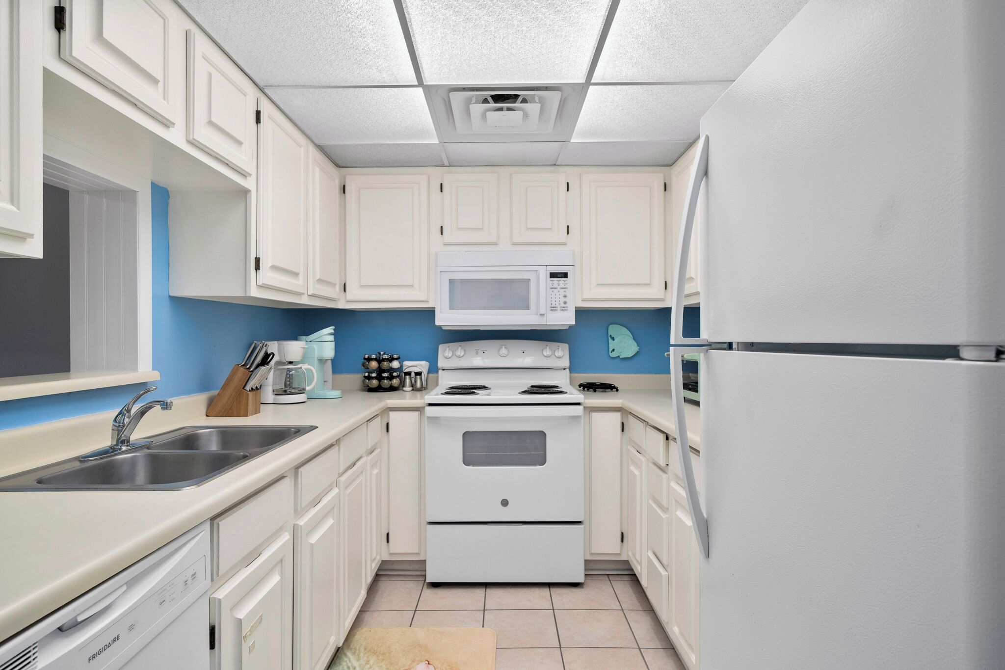A kitchen with white cabinets, a white stove, a microwave, and a refrigerator.