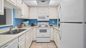 A kitchen with white cabinets, a white stove, a microwave, and a refrigerator.