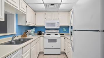 A kitchen with white cabinets, a white stove, a microwave, and a refrigerator.