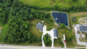 An aerial view of a residential area with a large house, a pond, and a road.