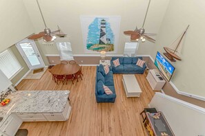 Un'ampia zona giorno con tavolo da pranzo, divani, ventilatori a soffitto e un grande quadro raffigurante un faro.