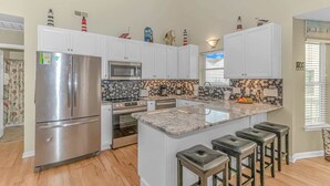 A modern kitchen with white cabinets, stainless steel appliances, a granite countertop, and a small island with stools. - Ocean Lakes 1076 (Myrtle Beach)