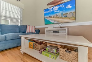 Ein Wohnzimmer mit blauem Sofa, einer weißen Unterhaltungseinheit mit Fernseher und Blick auf die Stadt.