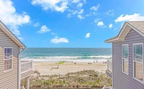 Blick auf einen Strand vom Haus aus, mit Balkon, dem Meer im Hintergrund und einem Sandstrand.