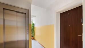 A hallway with a closed elevator, a wooden door with the number 81, and a potted plant. - Targówek Homely Apartment (Warszawa)