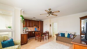 A living room with a sofa, chairs, a coffee table, a TV, and a kitchen area with cabinets and a ceiling fan. - Targówek Homely Apartment (Warszawa)