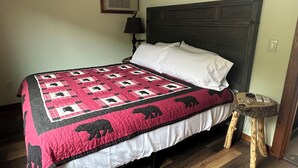 Una cama con colcha de motivos animales, una lámpara de noche y una mesita de madera.
