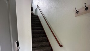 Una escalera con peldaños alfombrados y barandilla de madera, que lleva a un rellano con una puerta blanca y una pequeña mesa de madera.