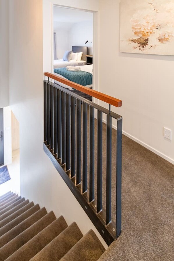 A staircase with a wooden handrail and metal balusters leading to a bedroom with a bed and a nightstand.